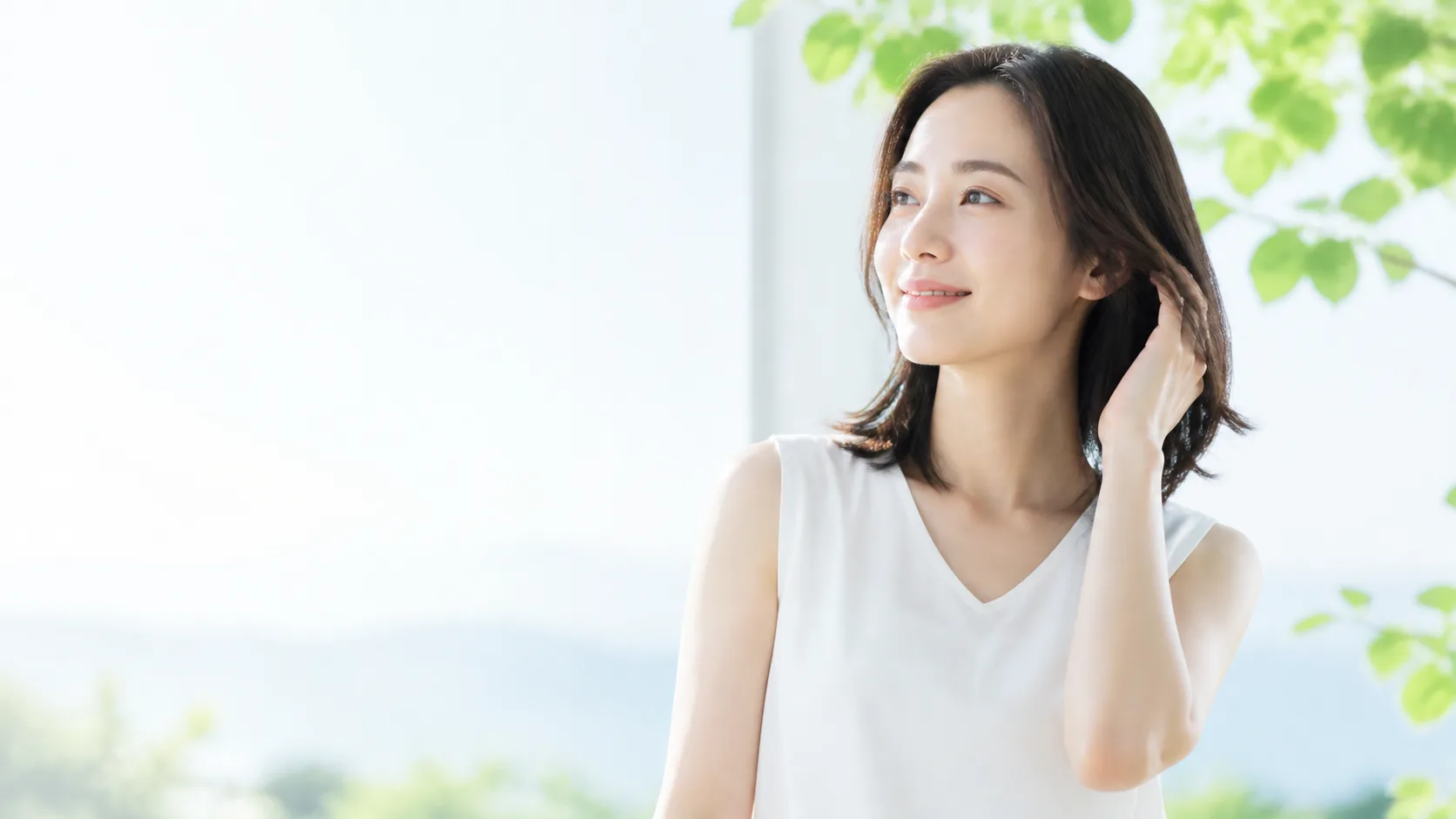 明るい自然光の中で髪に触れる女性